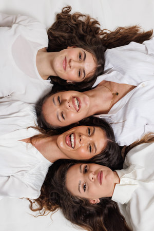 Group portrait of four young women smiling happily while lying together in a creative and harmonious arrangementの写真素材