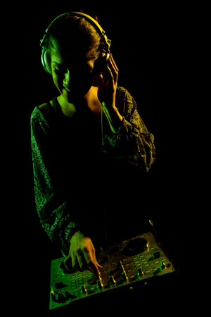 Female DJ with headphones on a mixer. Side lit silhouette of a girl playing techno music against...