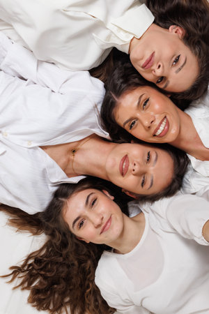 Four women in white shirts lying close, smiling and posing happilyの写真素材