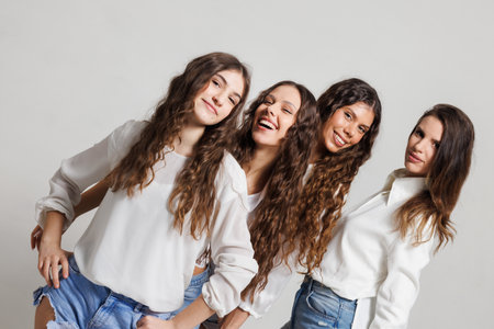Group of four cheerful women posing together in casual clothing against a neutral backgroundの写真素材
