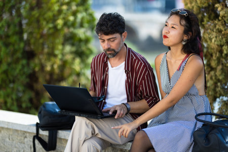 Young professionals collaborating outdoors, working on a laptop together in a sunny park setting, enjoying teamwork and creative brainstorming in a relaxed and natural environmentの写真素材