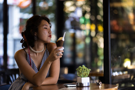 Woman enjoying an ice cream cone in a cafe while relaxing in casual summer attire with a serene expressionの写真素材