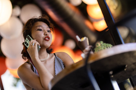 Young woman talking on smartphone in a cafe, enjoying a dessert, surrounded by warm ambient lighting...
