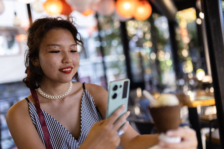 Young woman enjoying ice cream at a cafe while using her smartphone for taking a picture. Capturing...