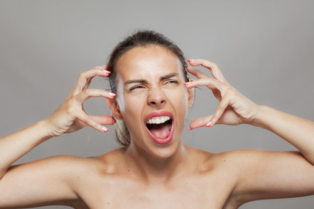 Expressive young woman screaming and clutching her face with manicured handsの写真素材