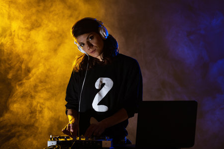 Female DJ on a mixer. Girl playing texhno music against smoke background.