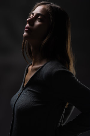 Elegant young woman in a dark studio setting, dramatic lighting and thoughtful expressionの写真素材