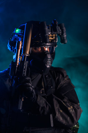 Tactical operative in night vision gear holding weapon in smoky ambianceの写真素材