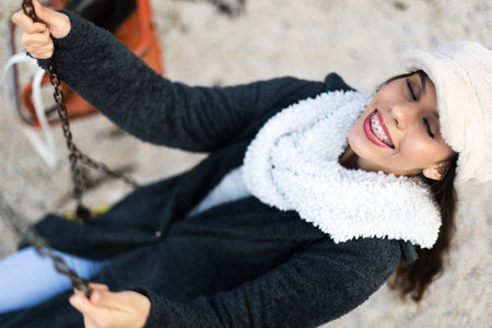Young woman with braces smiling on a swing during a cold day outdoorsの写真素材