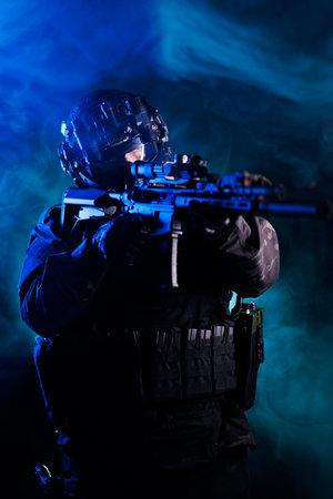 Soldier wearing tactical gear aiming a rifle amidst moody atmospheric lightingの写真素材