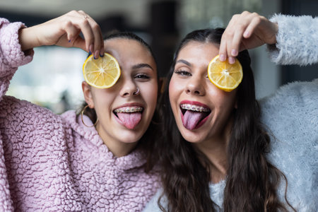 Two cheerful friends posing with lemon slices indoors, smiling playfullyの写真素材