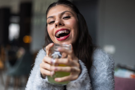 Happy woman with braces enjoying a drink in a cozy indoor settingの写真素材