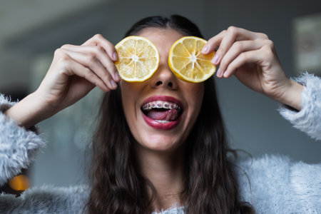 Playful young woman holding lemon slices over her eyes and smiling widelyの写真素材