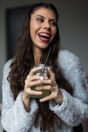 Cheerful Young Woman Enjoying a Beverage While Smiling and Relaxing Indoorsの写真素材