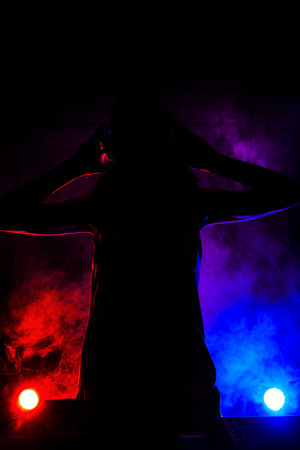 Silhouette of a girl DJ playing music on a mixer. Red and blue lights and smoke in the backgroundの写真素材