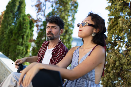 Casual outdoor interaction between two friends enjoying a sunny day in a park setting, with trees in the background creating a serene and relaxed atmosphere.の写真素材