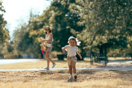 Young Child Running Outdoors While Parent Observes in a Sunny Park Settingの写真素材