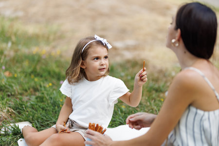 Mother and daughter enjoying a picnic together in a sunny green parkの写真素材