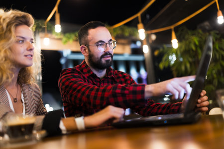 Collaborative team working on a laptop in a modern cafe environment with string lights, discussing...