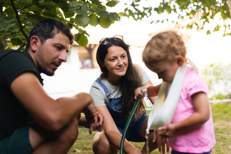 Young family enjoying outdoor time, engaging with their child during a playful garden activity under leafy treesの写真素材