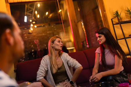 Group of friends enjoying casual conversation in a cozy living room with warm lighting in the...