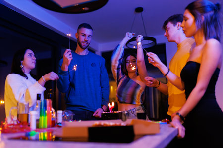 Group of friends celebrating joyfully with sparklers during a festive evening indoors