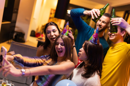 Friends celebrating at a party wearing party hats and enjoying drinks togetherの写真素材
