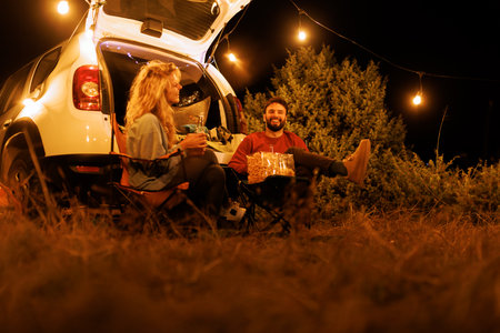 Enjoying a cozy night under the stars with friends by the car, surrounded by nature and warm lights