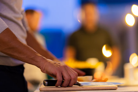 Close-up of hands cutting vegetables during a vibrant gathering in a warmly lit kitchen