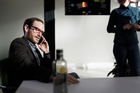 Businessperson engaged in a phone conversation during a meeting in a modern office setting with a...