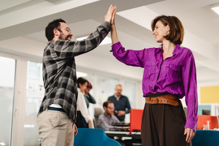Business professionals celebrate success with high five in modern office during team meeting,...