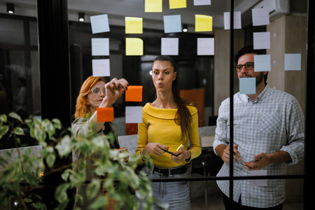 Team collaboration and brainstorming session at a modern office with sticky notes on glass wall