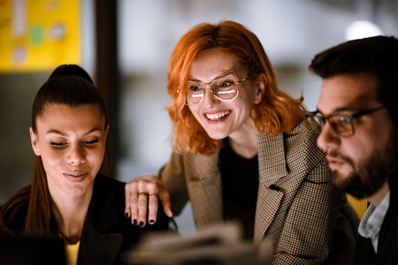 Group of smiling professionals collaborating in a modern workspace during evening hoursの写真素材