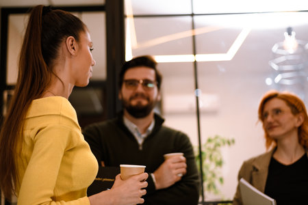 Group discussion in a modern office setting with three professionals engaging during a coffee break in the afternoonの写真素材