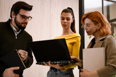 Group of professionals collaborating in a modern office space while discussing project details on a laptop during daylight hoursの写真素材