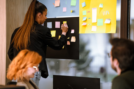Team brainstorming session in a bright office with sticky notes on the wall during the afternoonの写真素材