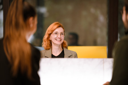 Friendly receptionist greets clients with a warm smile at a modern office during the day, creating a welcoming atmosphere for visitorsの写真素材