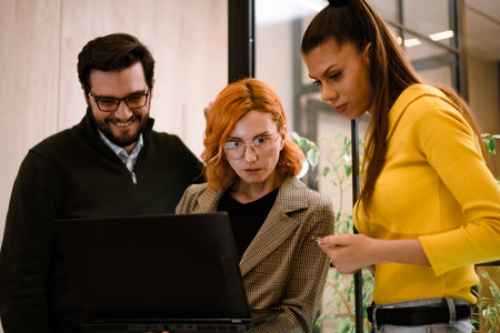 Team collaboration in a modern office setting while discussing project details on a laptop during work hoursの写真素材