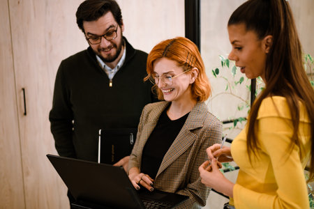 Team members collaborating in a bright office, discussing ideas while looking at a laptopの写真素材