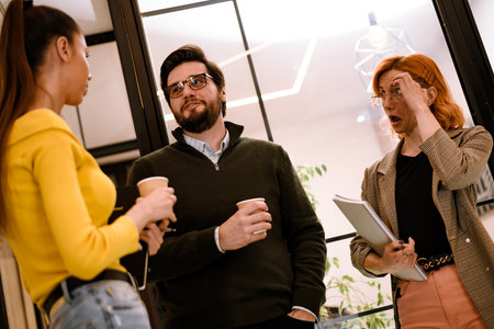 Two women and a man discuss ideas while enjoying coffee in a modern office space during a working session on a productive afternoonの写真素材