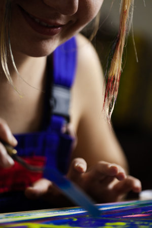 Close-up of a young female artist using bright paint colors on canvas, showcasing creativity and artistic expression in her workspace.の写真素材