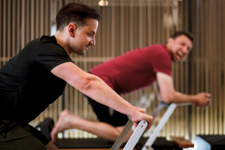 Men engaging in workout sessions on reformer pilates machines at a fitness studio during a morning class for improved strength and flexibilityの写真素材