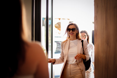 Group of stylish women entering a modern building during daytime, showcasing casual elegance and cheerful expressions as they interactの写真素材