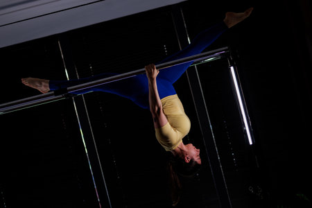 Pole dancer performs an impressive inverted pose during an indoor training session in a brightly lit...