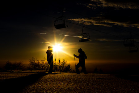 Silhouetted skiers at sunrise near ski lift in picturesque winter landscape