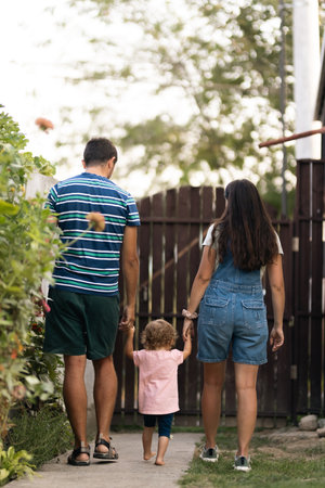 Parents walking with their young child through a garden pathway during a sunny day.の写真素材