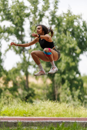 Young woman performing a dynamic jump outdoors on a sunny day, showcasing energy, fitness, and...