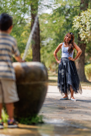 Woman laughing in a park beside a water fountain as a child plays nearbyの写真素材