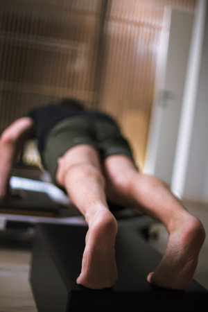 Man performing an advanced exercise on a reformer pilates machine in a modern studio during a morning workout sessionの写真素材