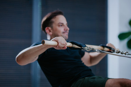 Man performs rowing exercise on reformer pilates machine in modern studio during morning workout...